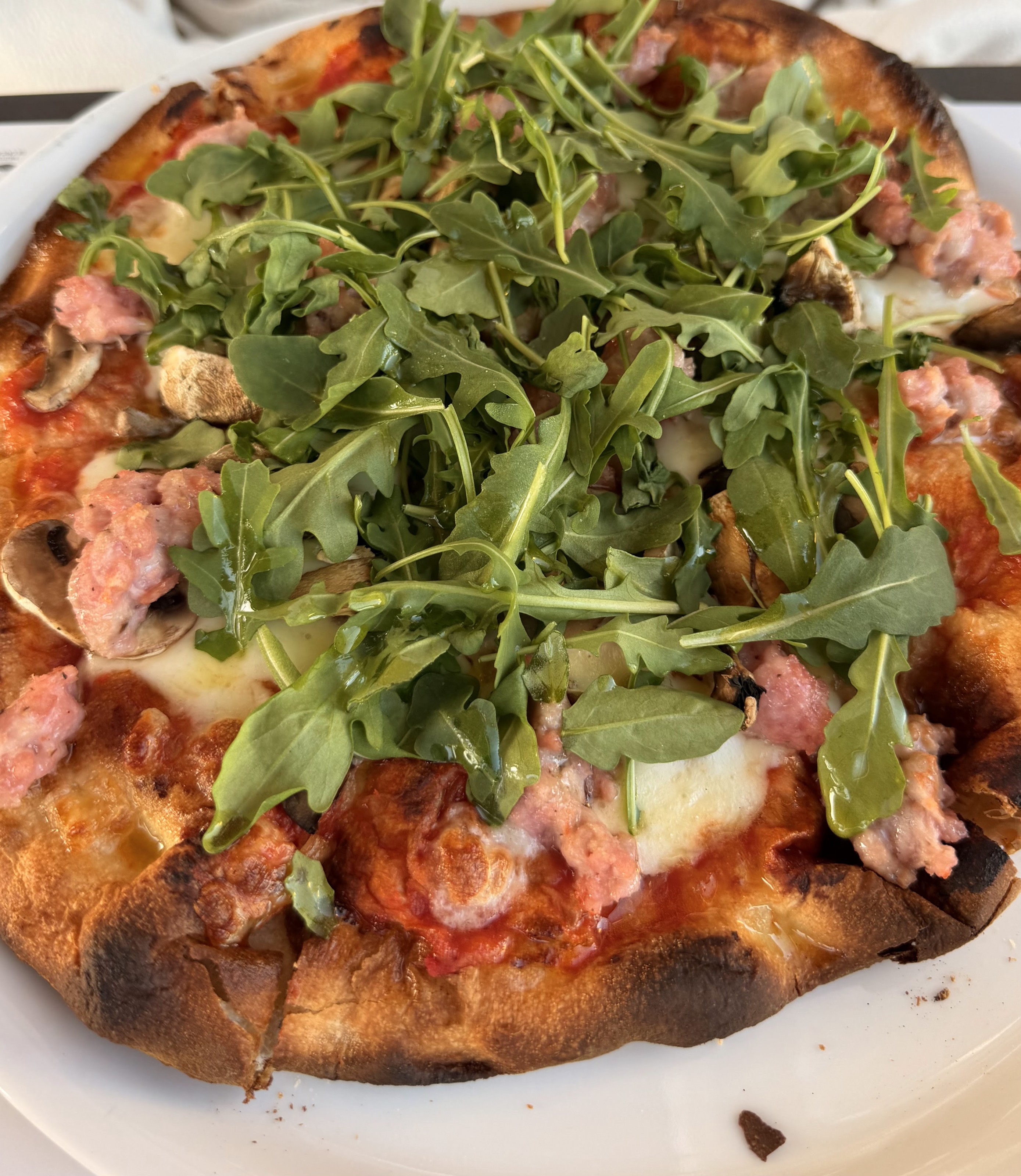 Pizza con salchicha, champiñones y mucha rúcula